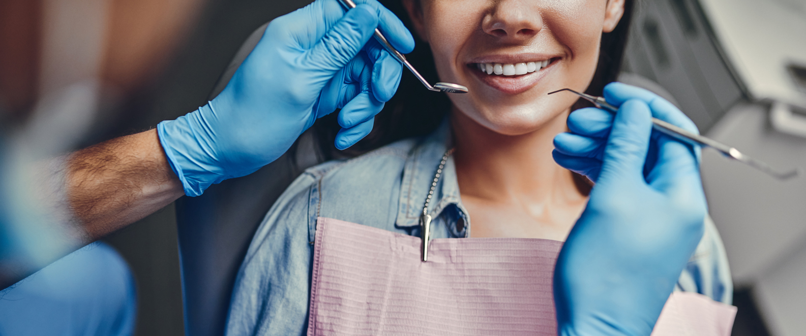 Patient smiling with a dental professional's gloved hands holding instruments beside their smile.